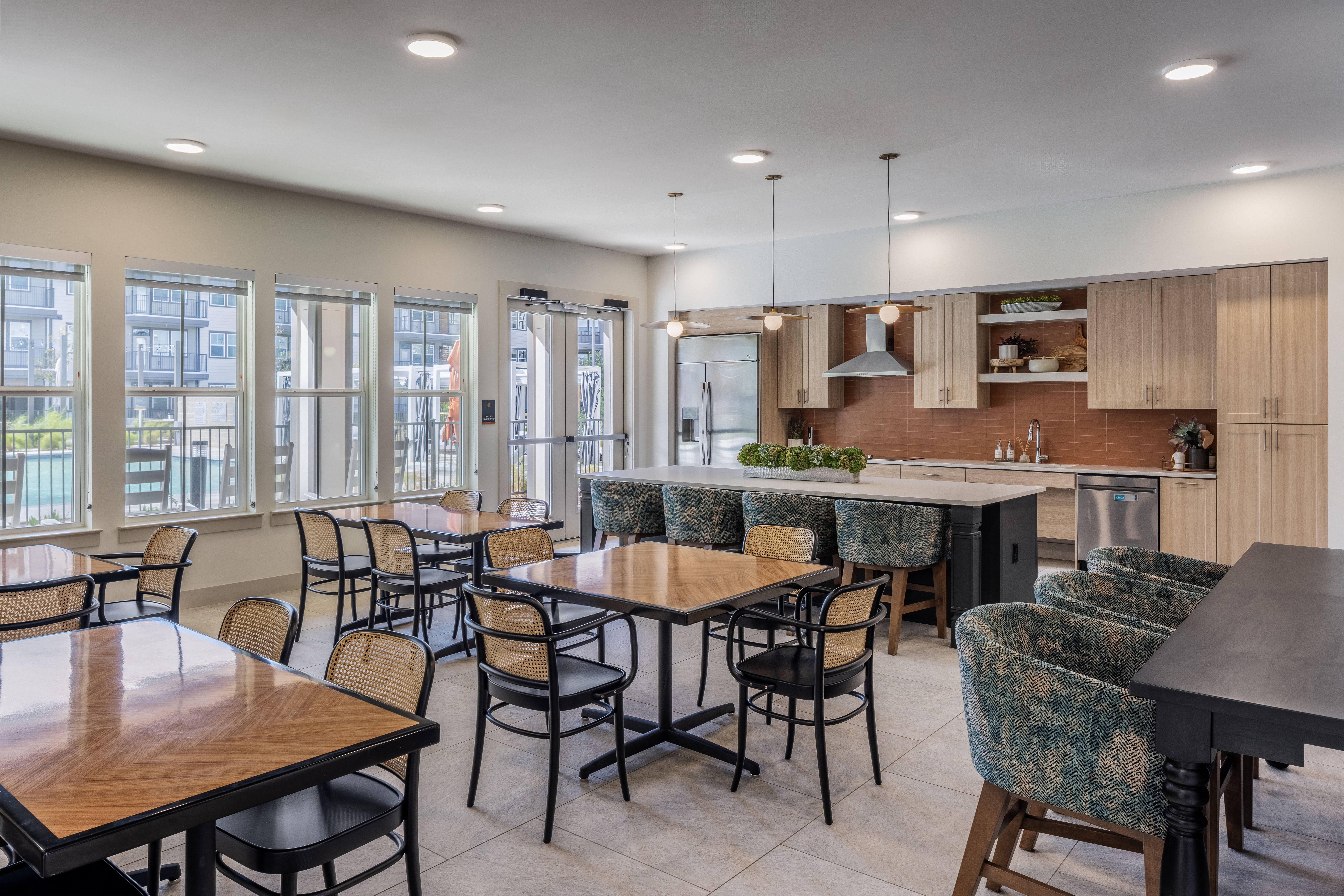 an open kitchen and dining area with tables and chairs and an island with seating at a senior apartment community